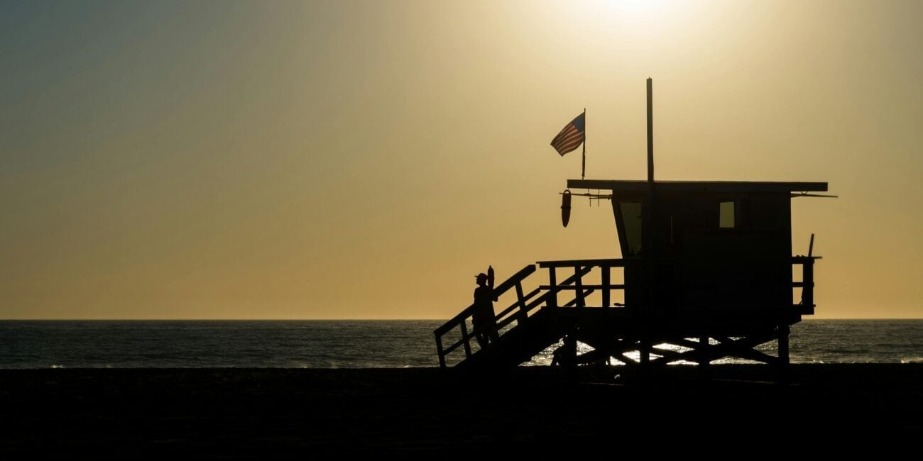 Silhouette of a lifeguard tower with an American flag on a beach during sunset.