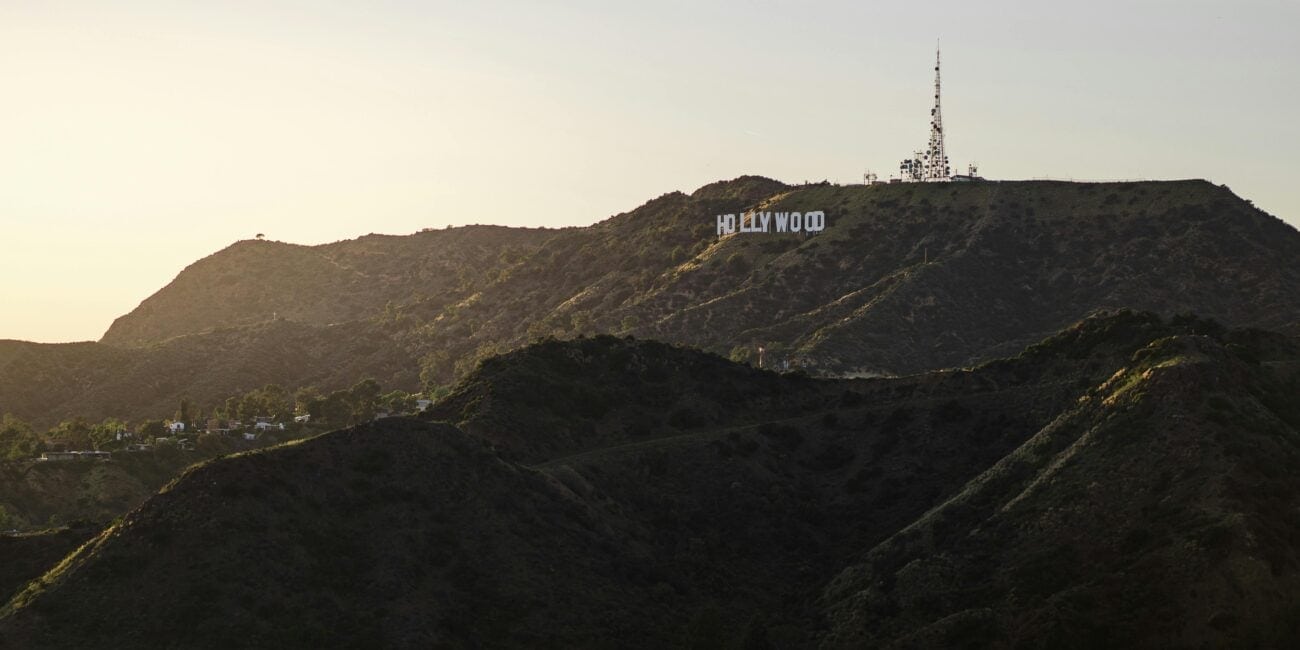 Hollywood sign on a hilly terrain with a communications tower above it, set against a clear sky at sunset.