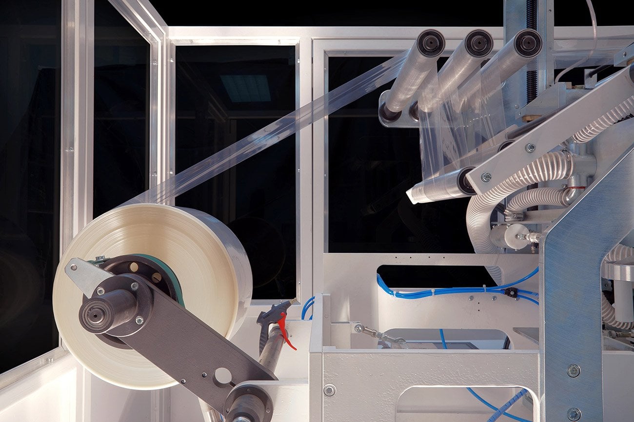 Industrial packaging machine winding plastic film onto rolls.