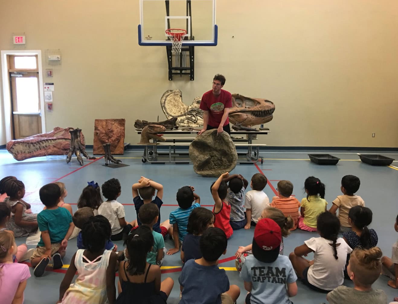 Dinosaurs Rock Instructor demonstrating a T-Rex Footprint to a group of campers with a variety of dinosaur specimens in the background