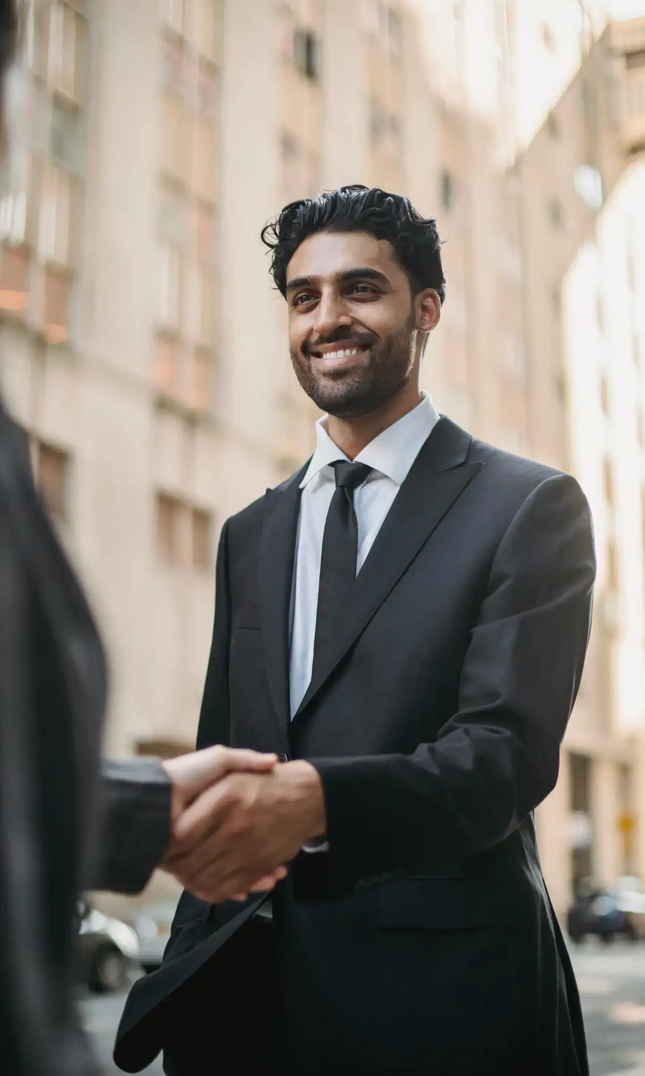 A smiling man in business attire handshaking another person