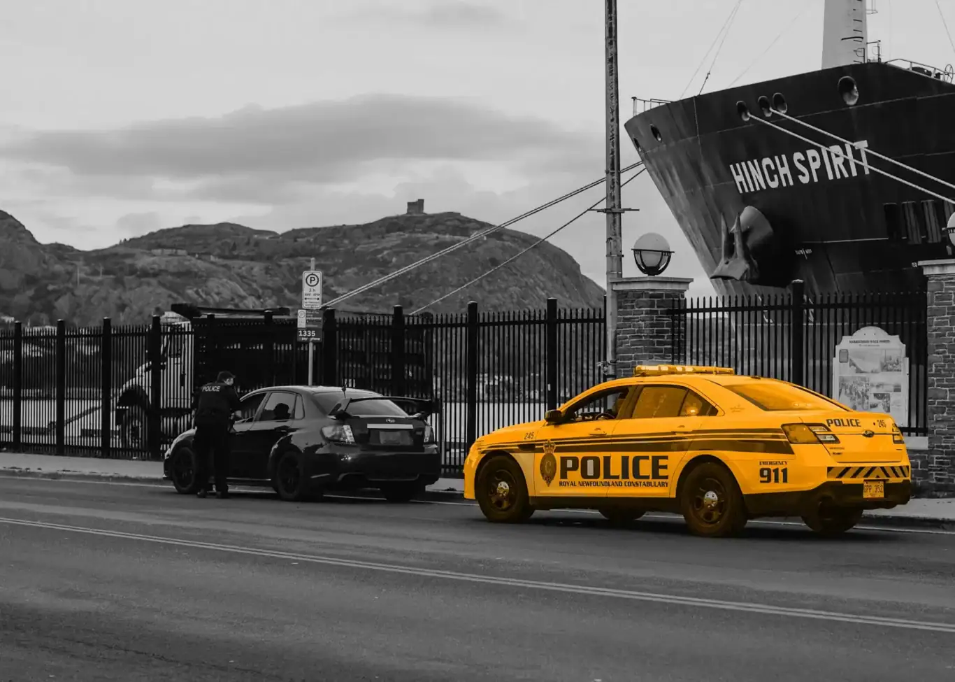 A black and white image of a car being pulled over by a orange police car