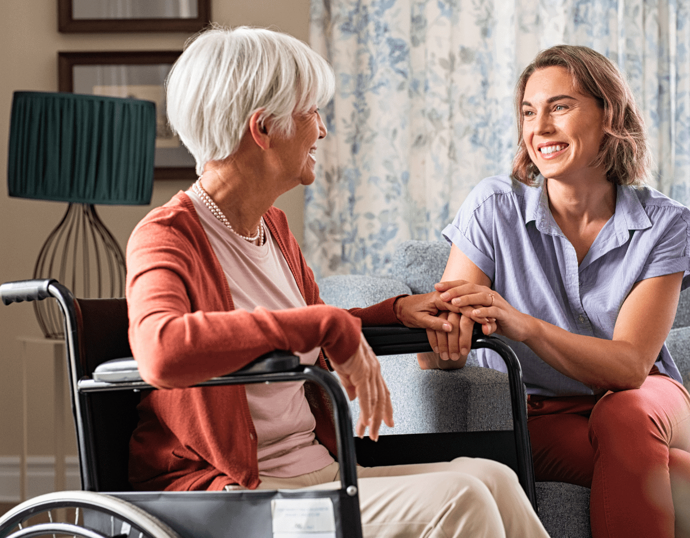 Smiling caregiver holding hands with a senior woman in a wheelchair, representing compassionate senior living support and personalized care.