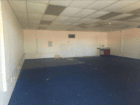 Empty office space with a blue carpet, scattered debris, and a small counter along the back wall.