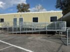 Beige, single-story building with large windows, surrounded by metal wheelchair ramps and rails in a parking lot under a blue sky.