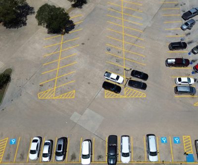 Aerial view of new yellow parking stalls, crosshatch islands, and ADA symbols at a shopping center in Madisonville, TX
