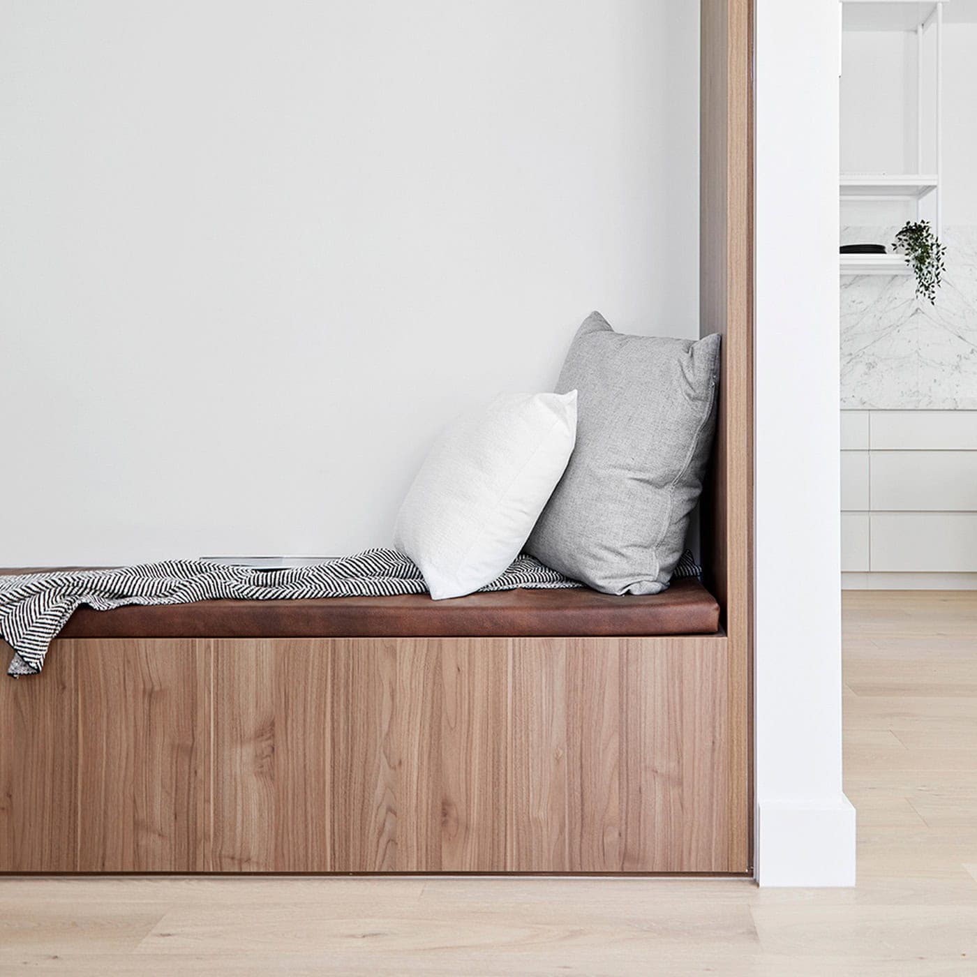 Built-in timber window seat with brown leather cushion, throw pillows, and striped blanket.