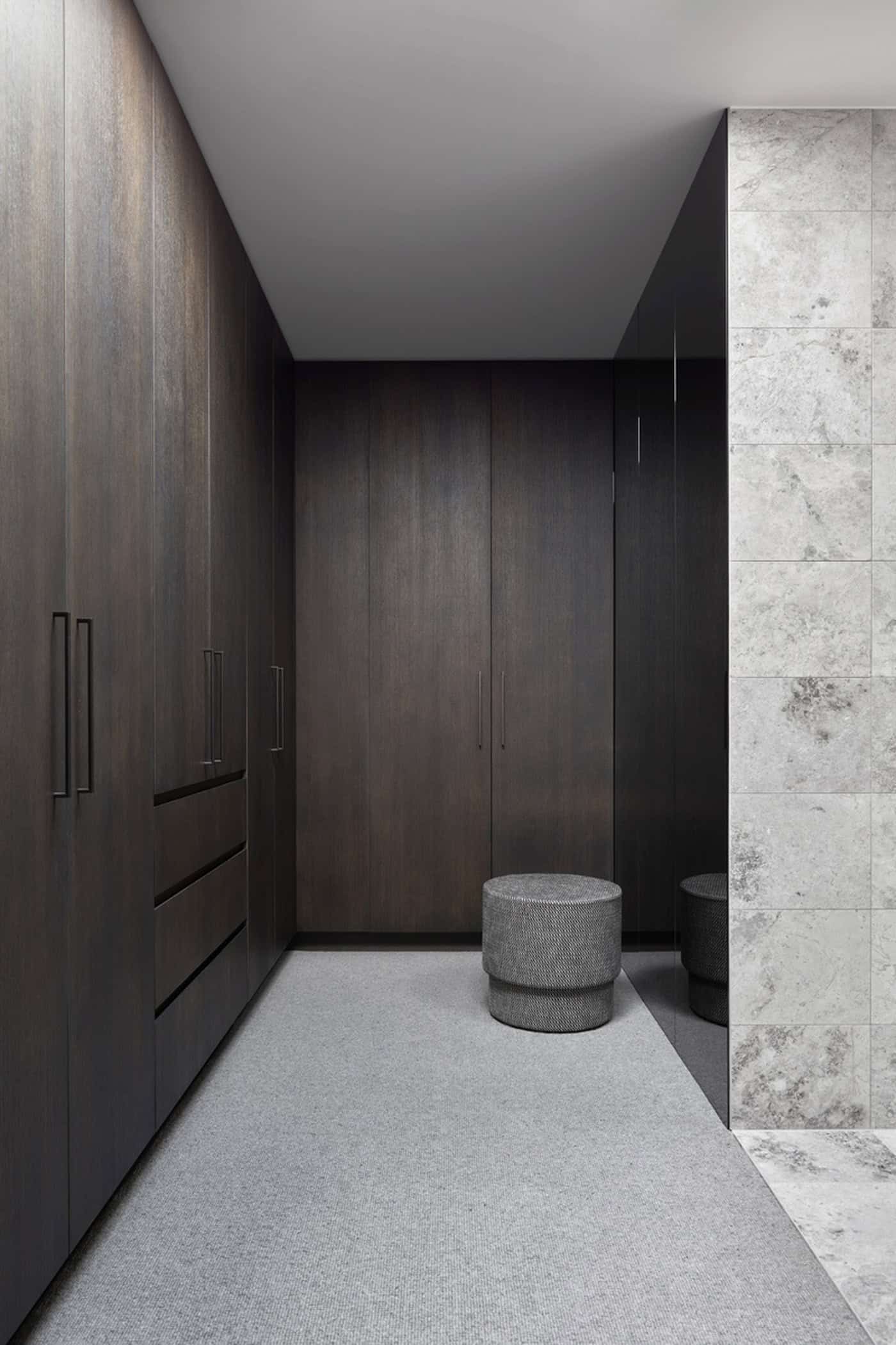 Luxurious walk-in wardrobe featuring dark timber built-in closets, grey carpet, and a ottoman.