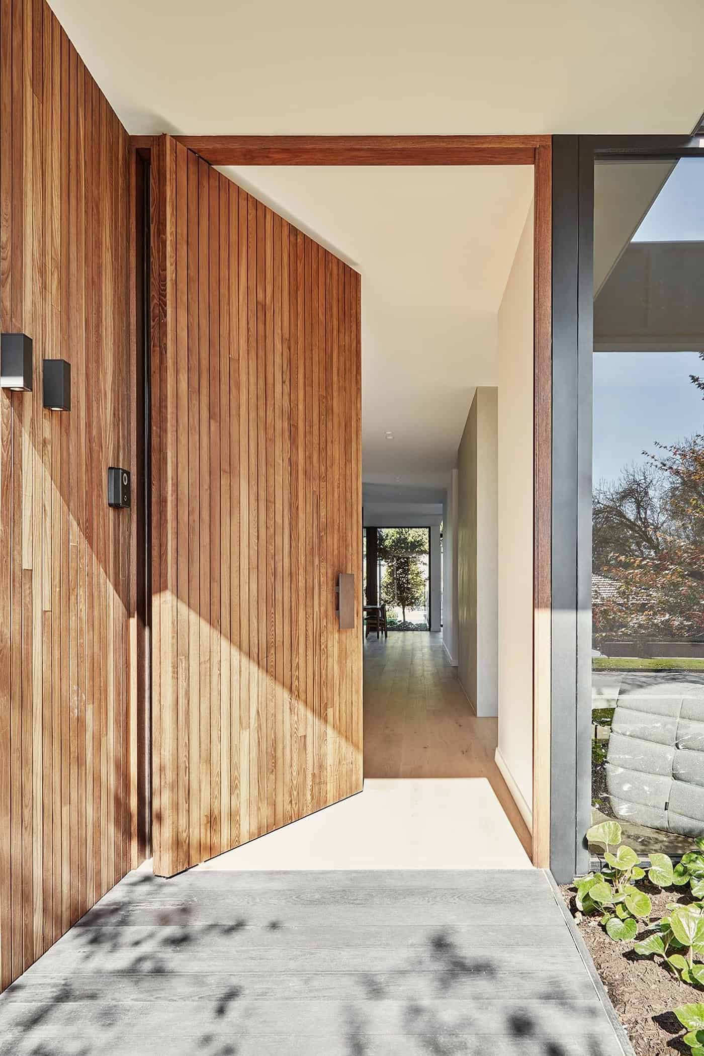 Large vertical timber slat pivot door open to a brightly lit entrance hallway.