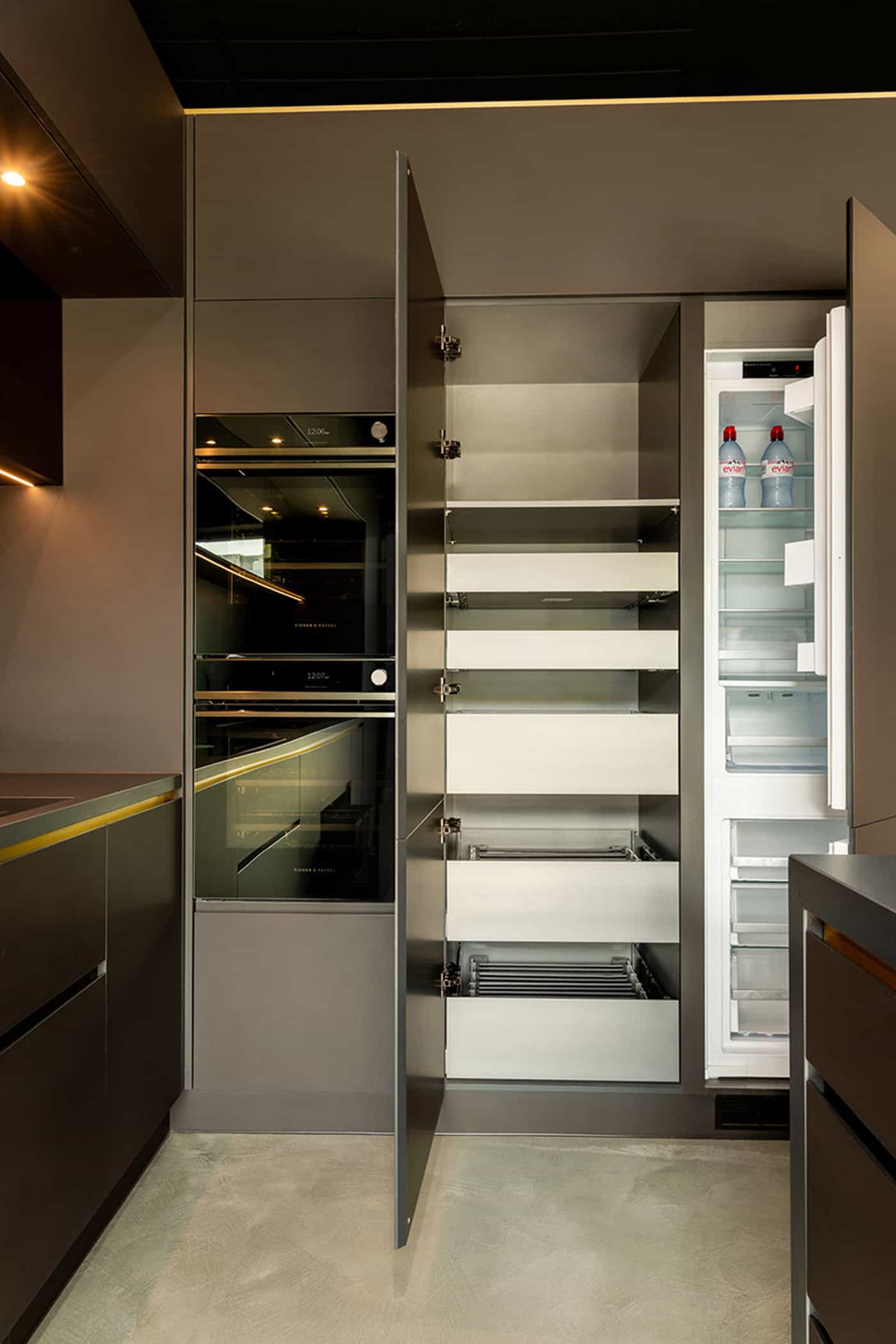 Open pantry unit with pull-out drawers alongside integrated wall ovens and fridge.