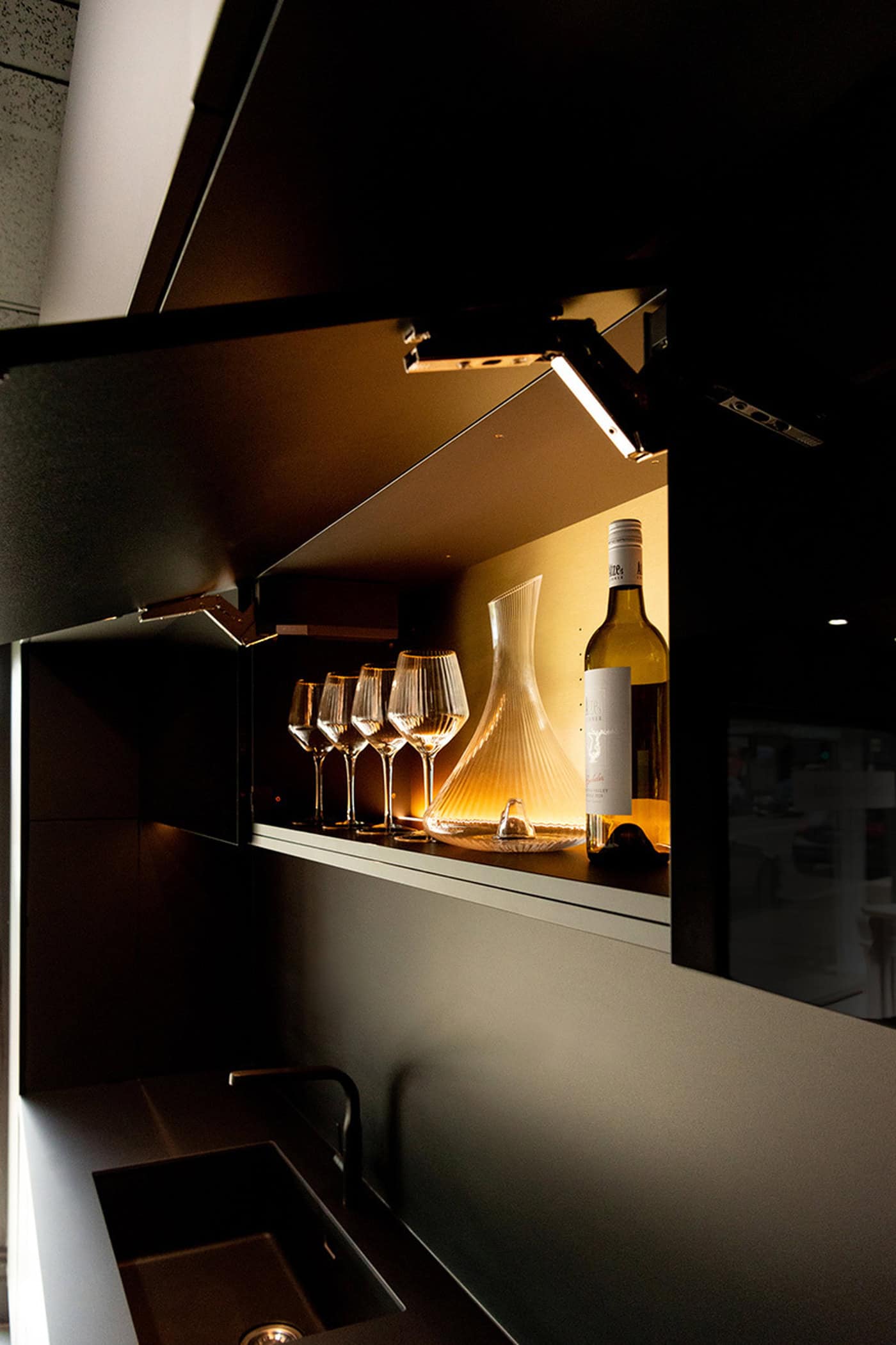 Illuminated upper cabinet storing wine glasses, a decanter, and a wine bottle.