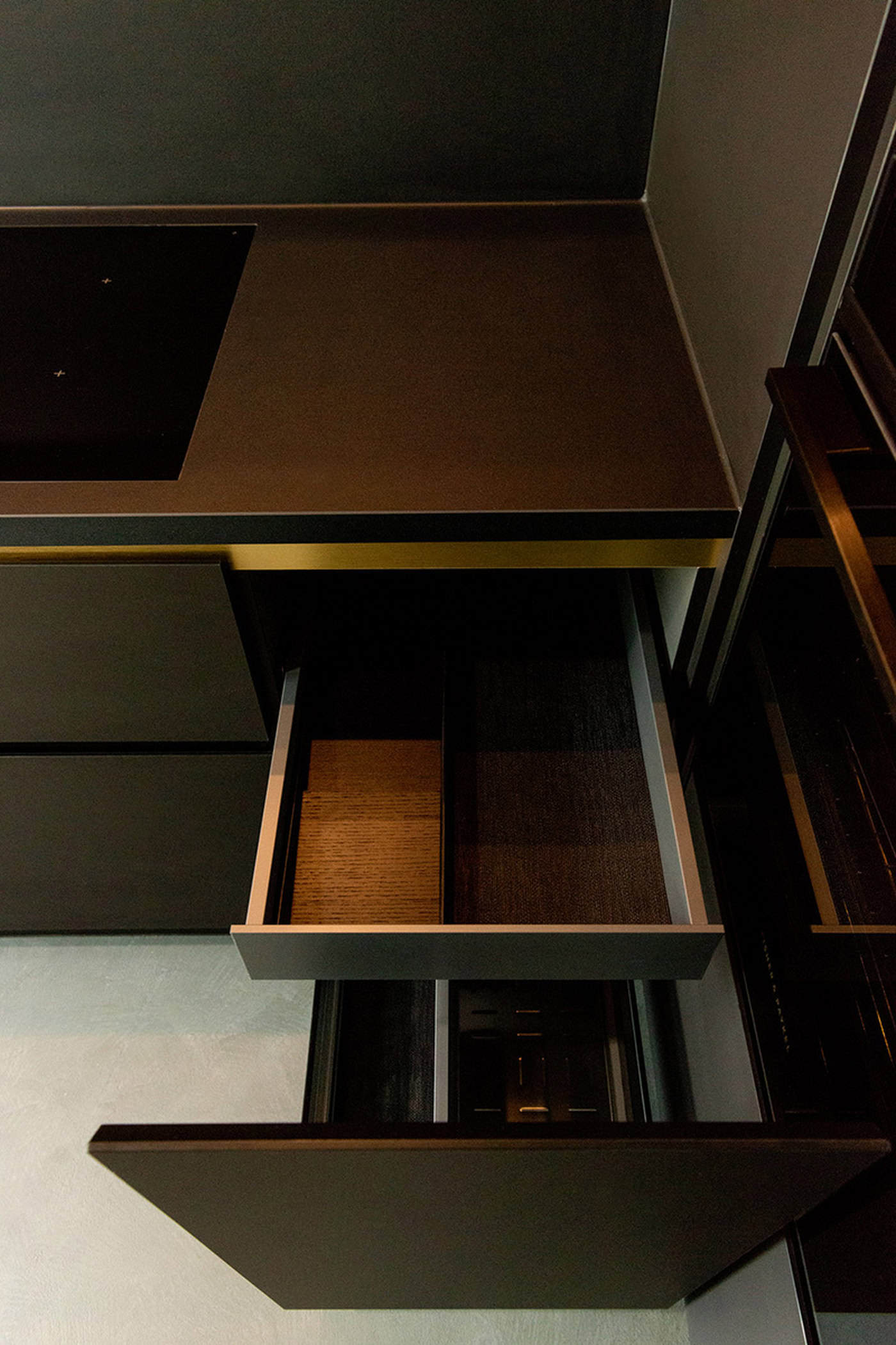 Open charcoal kitchen drawer revealing an internal hidden drawer and brass trim detail.