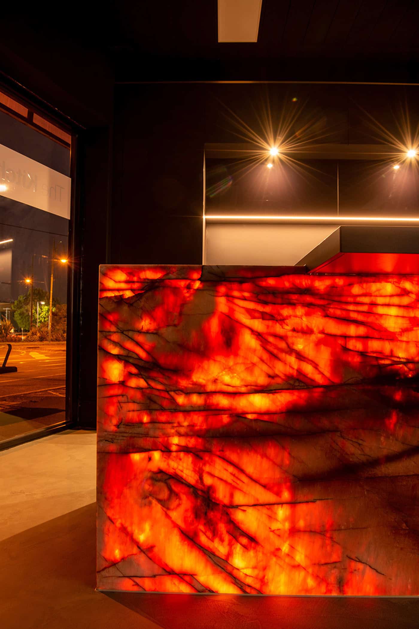 Vibrant red backlit onyx island bench panel featured in a modern luxury kitchen window display.
