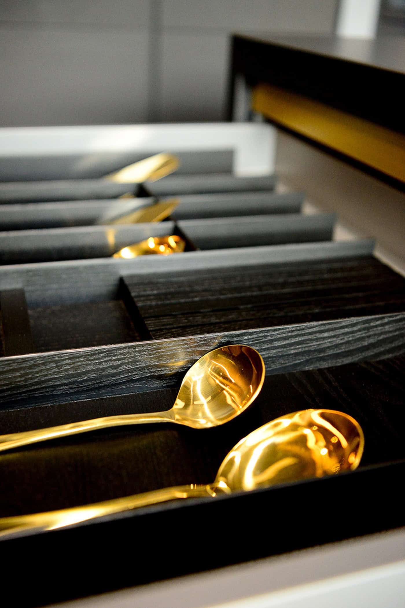 Gold cutlery stored neatly inside a custom dark wooden kitchen drawer organizer.