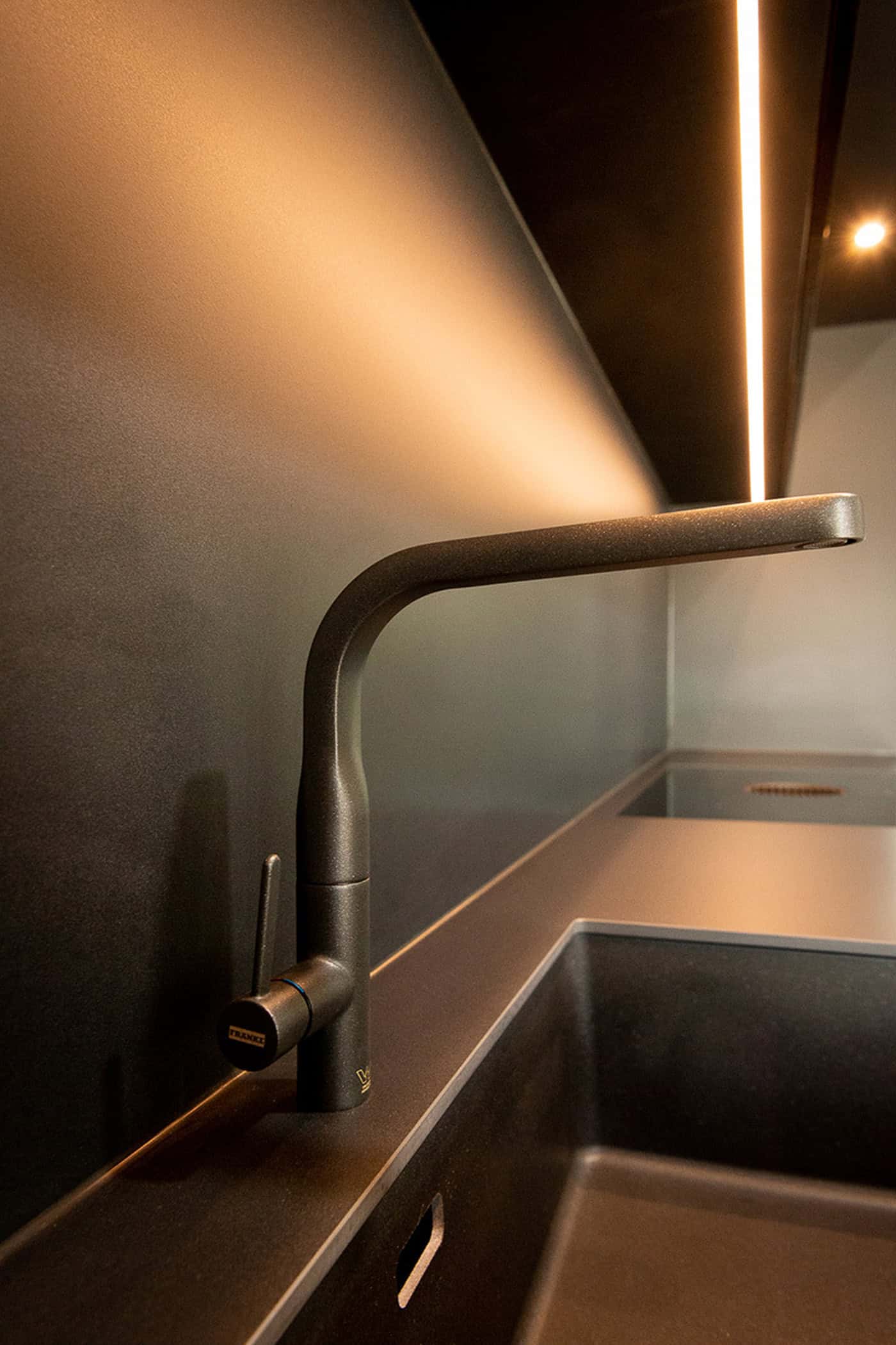 Matte black Franke tap set over an undermount sink with warm splashback lighting.
