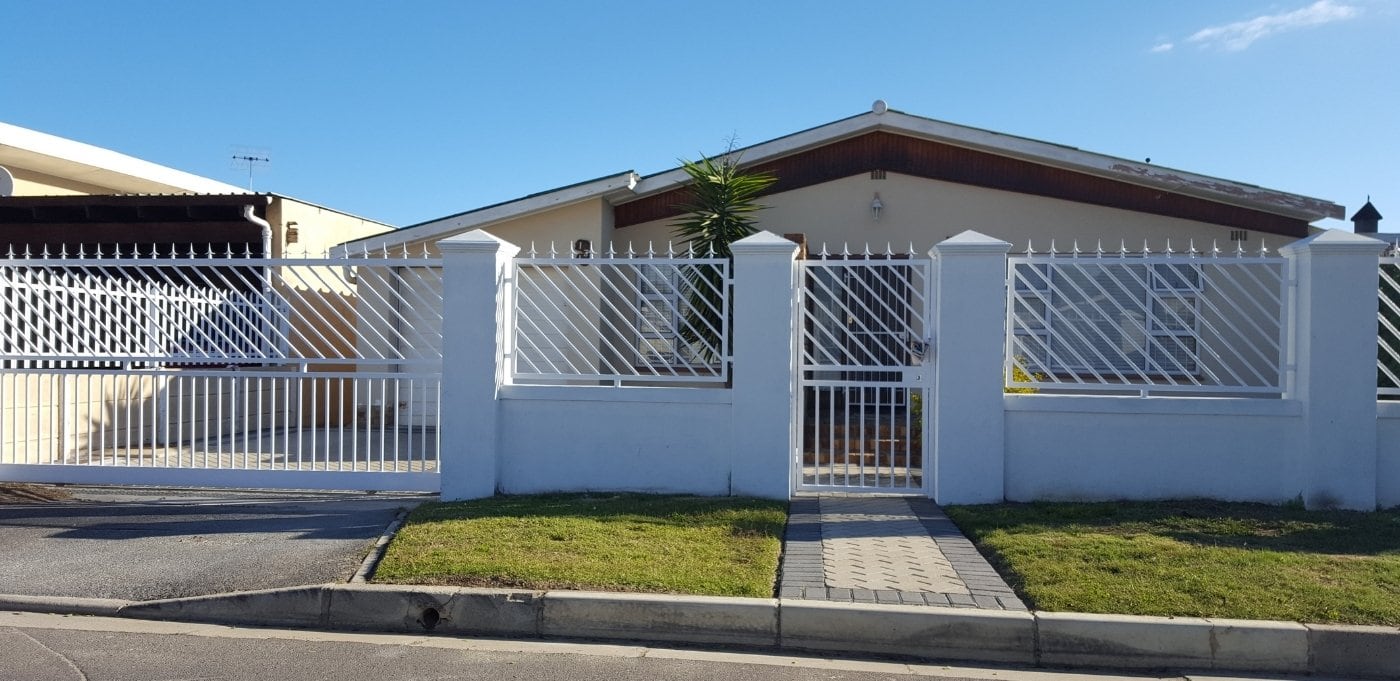 White custom driveway gate with matching fence panels and sharp spike tops securing the entrance of a suburban home.