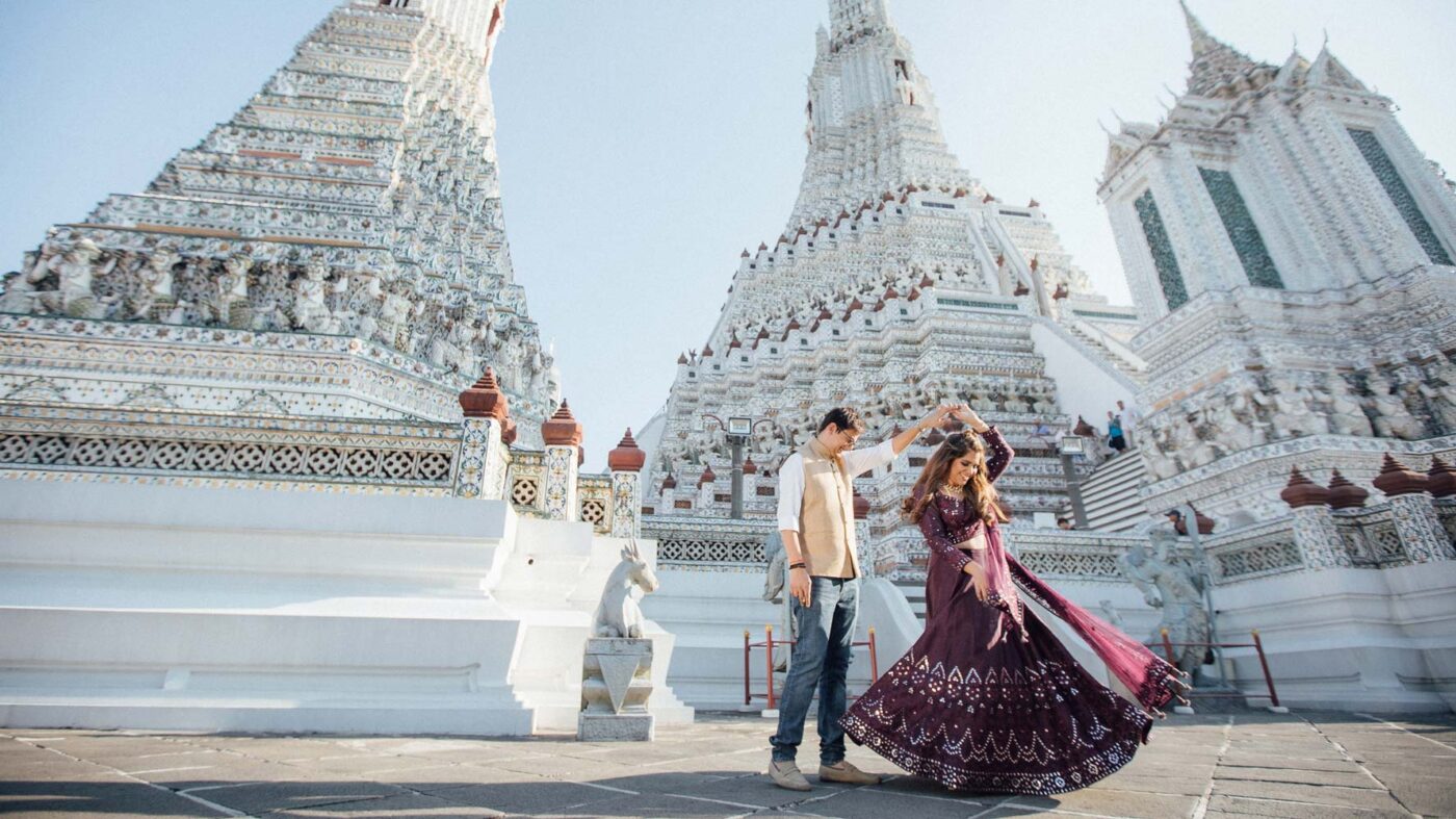 Couple dancing in front of the ornate white towers of Wat Arun in Bangkok