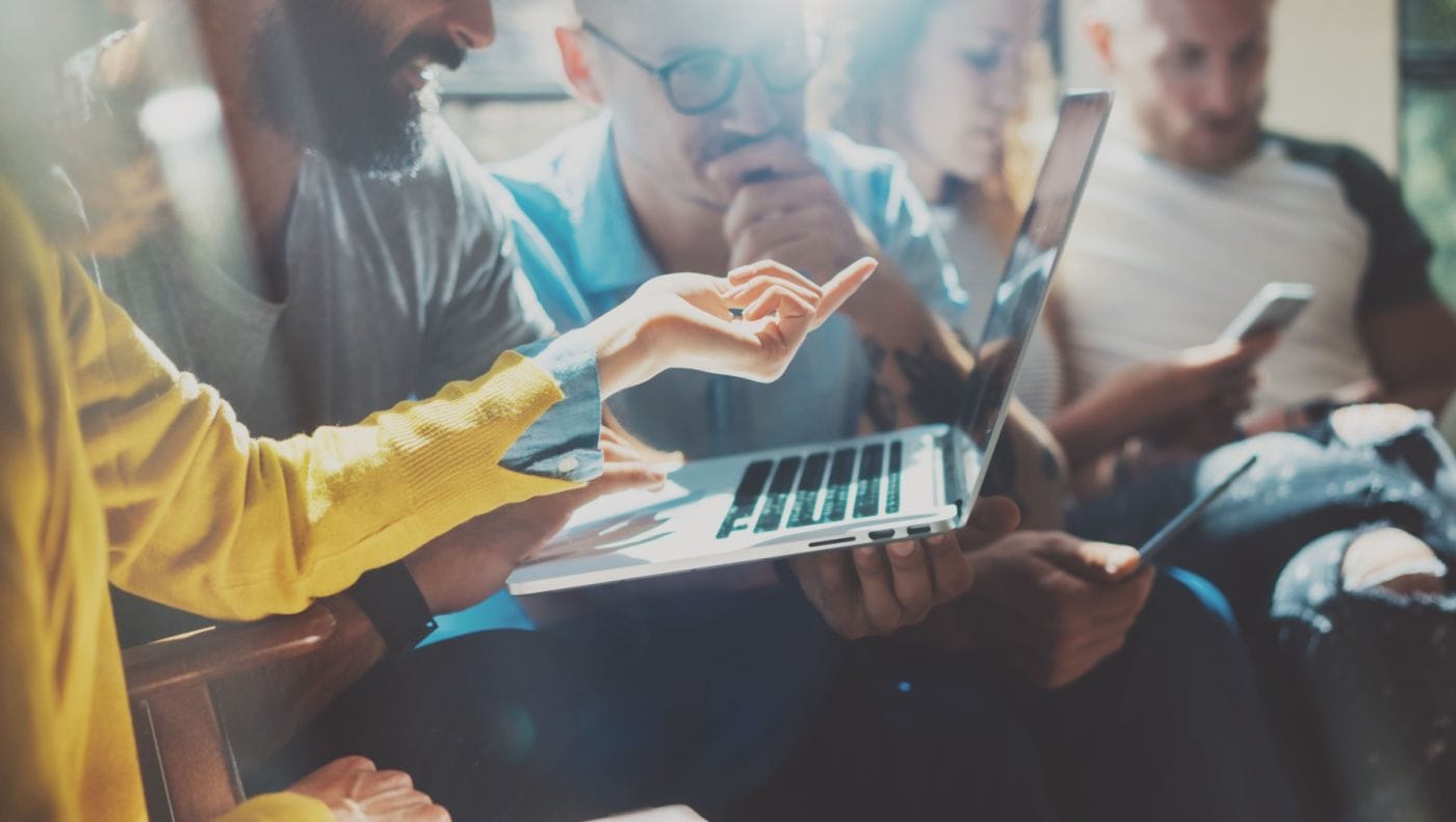 Três pessoas olhando para um notebook, enquanto uma delas explica uma apresentação