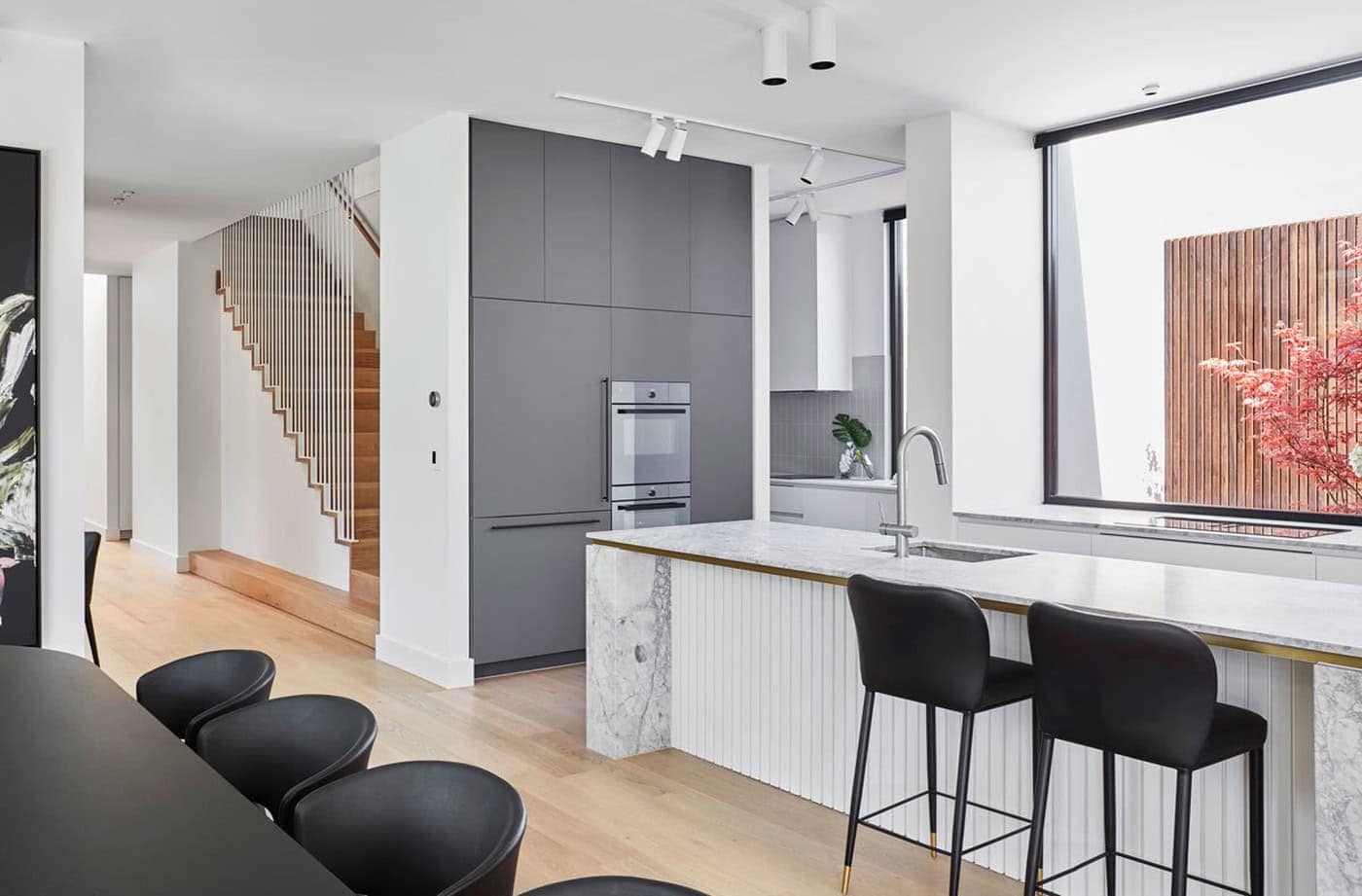 Open-plan kitchen and dining area with fluted marble island, dark cabinetry, and slatted wooden staircase.