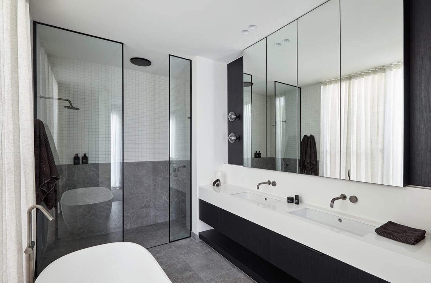 Modern bathroom with a double sink floating vanity, mirrored cabinets, walk-in shower, and freestanding bathtub.