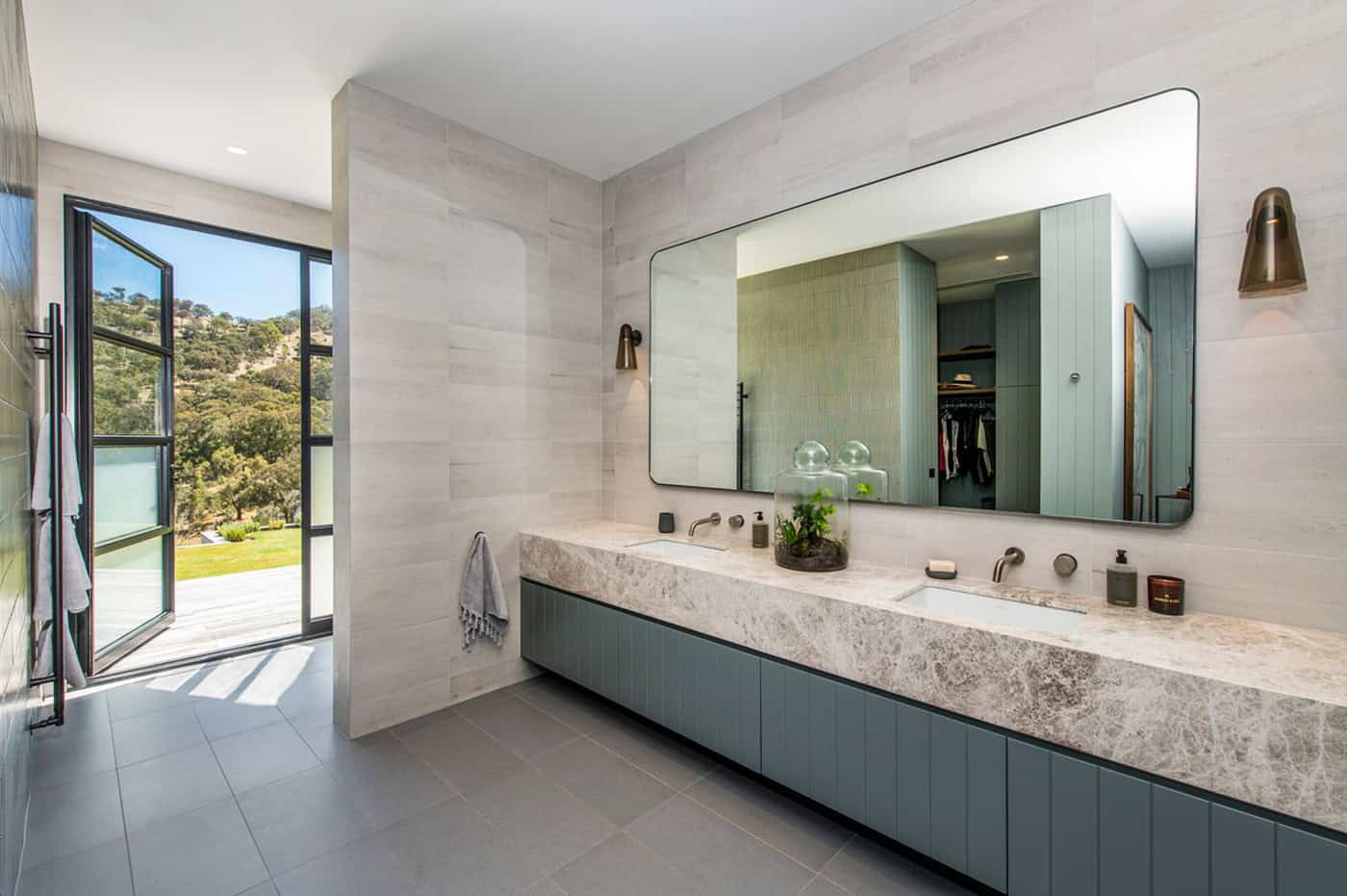 Spacious bathroom with marble double vanity, blue-grey cabinetry, large mirror, and open door to view.