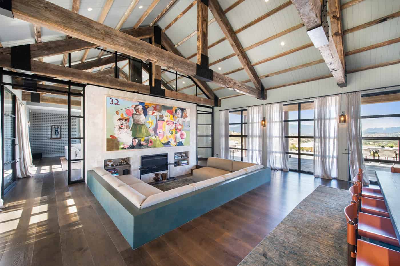 Sunken lounge with built-in seating, exposed timber beams, artwork, and large glass windows.