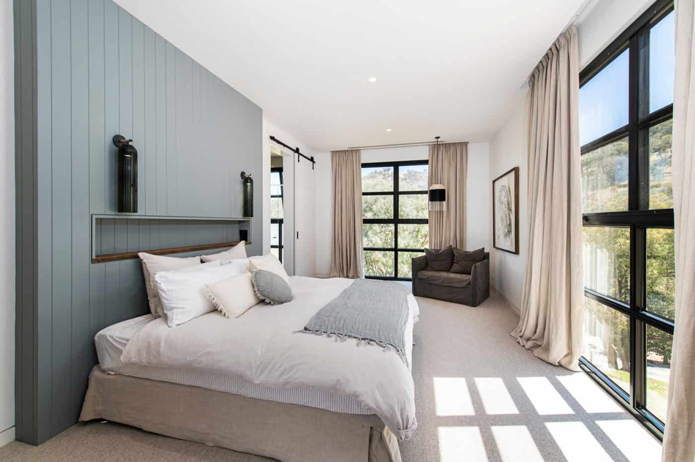 Bright primary bedroom with sage green paneled headboard wall, floor-to-ceiling windows, and drapes.