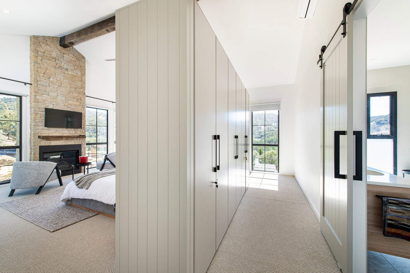 Master bedroom suite with built-in wardrobes, barn door, and a stone fireplace in the sleeping area.