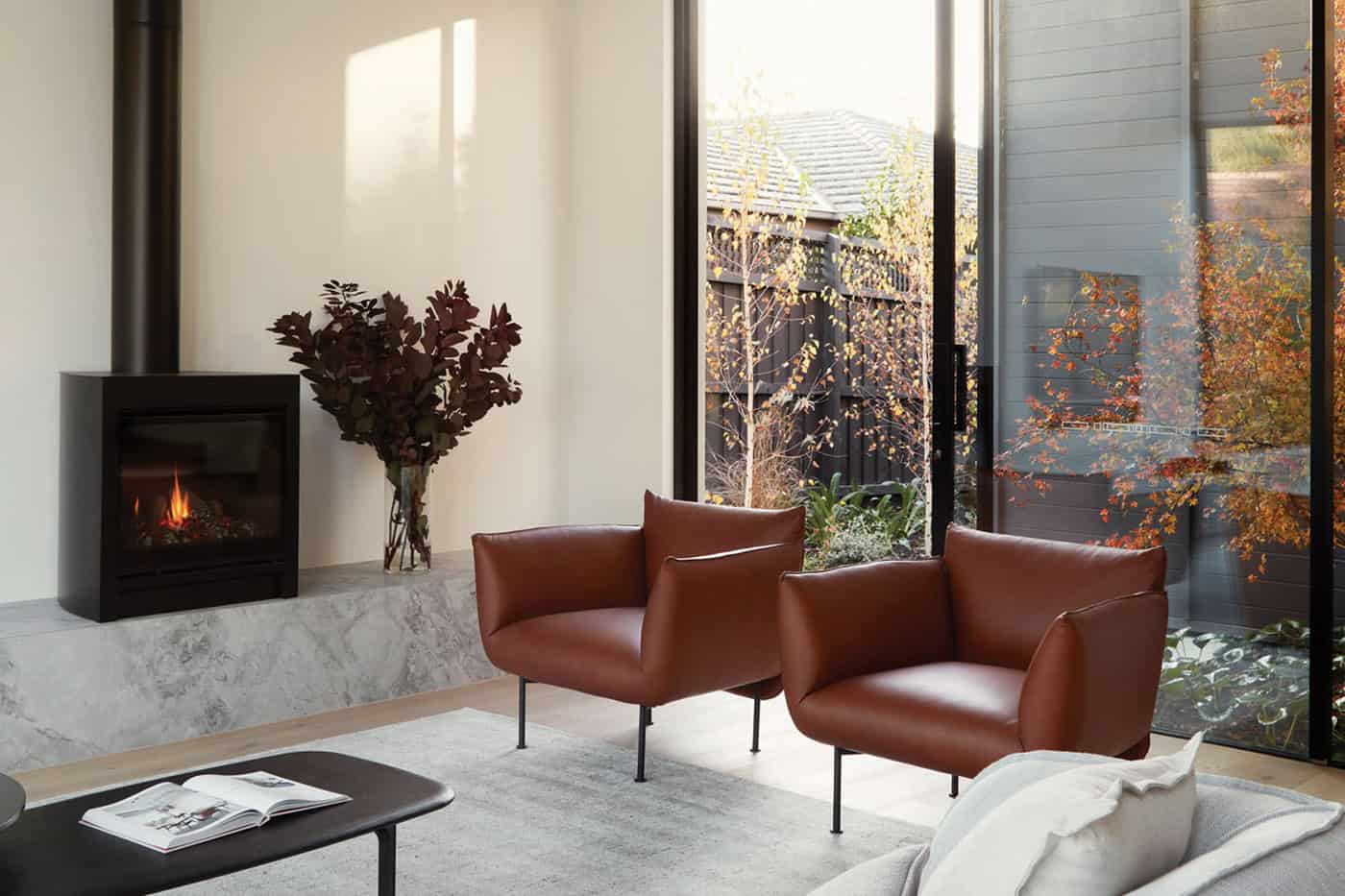  Cozy sitting corner with two cognac leather armchairs, black modern fireplace, and floor-to-ceiling glass door.