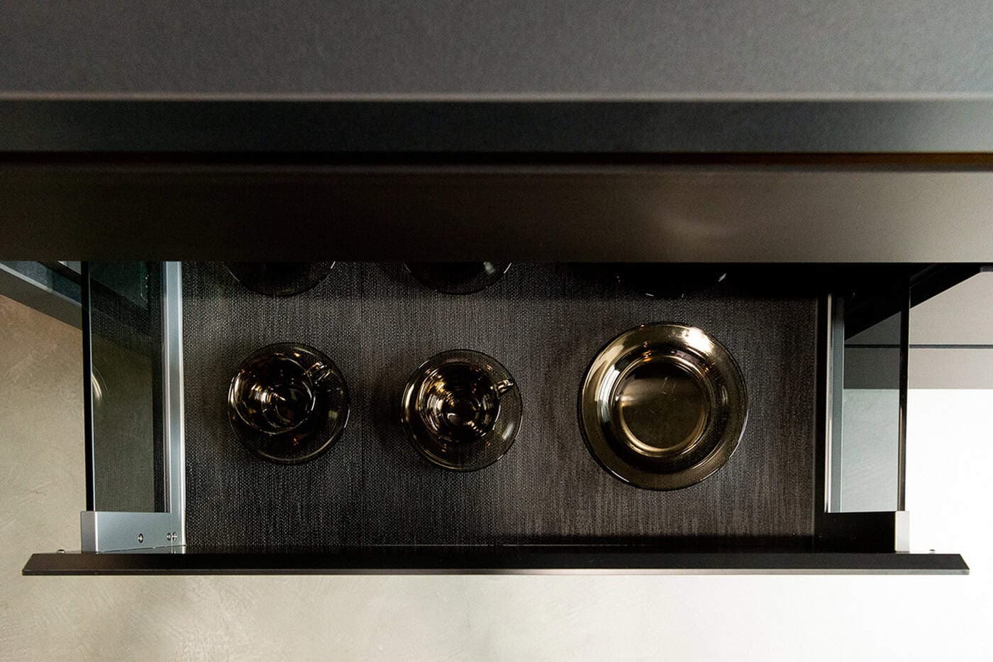 Overhead view of an open dark kitchen drawer with glass side panels holding tea sets.
