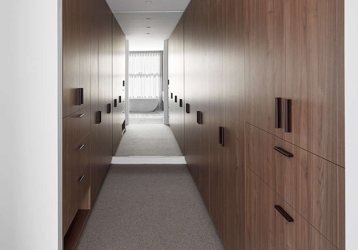 Walk-through robe featuring floor-to-ceiling dark timber wardrobes leading to an ensuite bathroom.