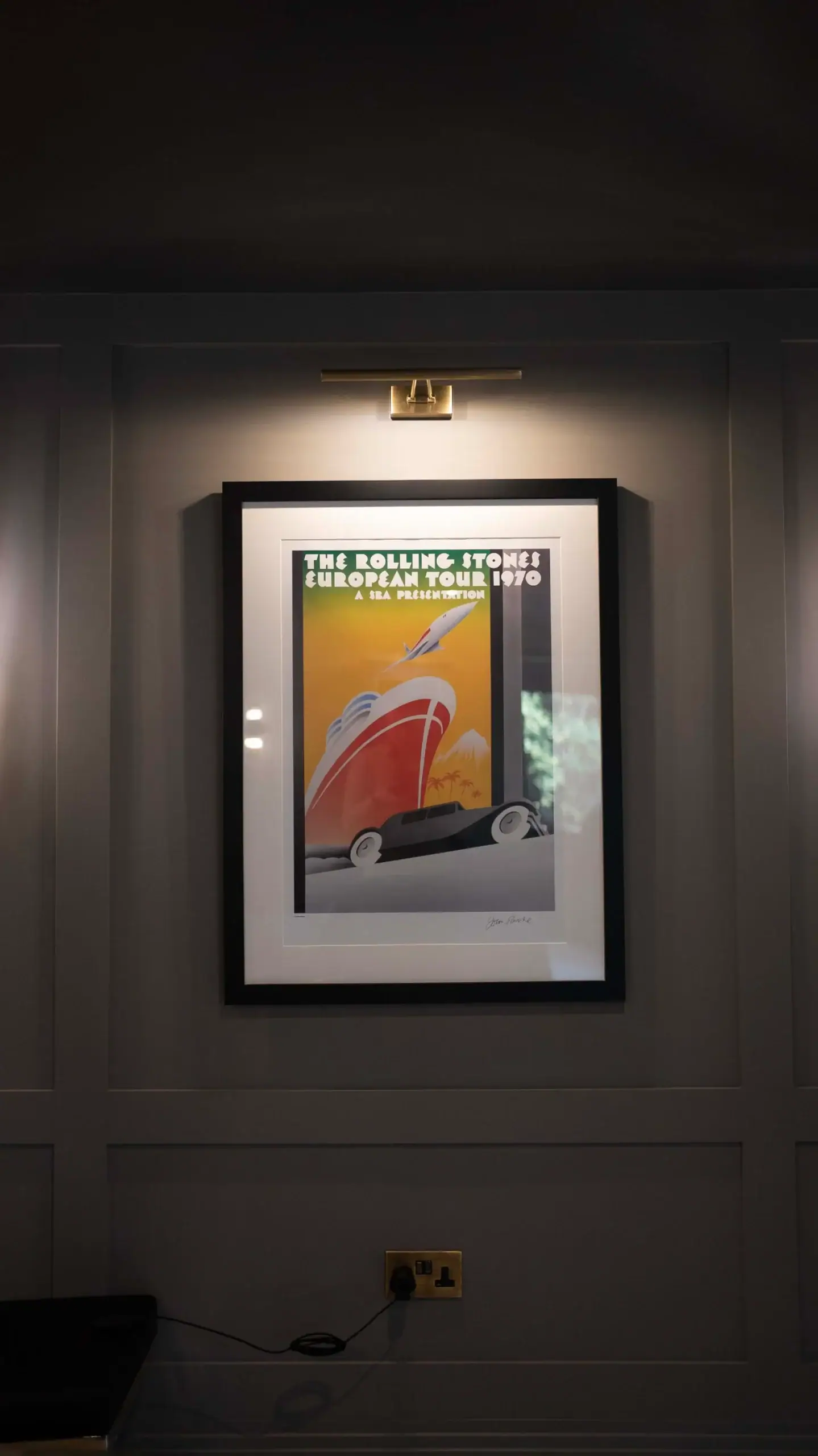 Framed poster lit by a picture light on a panelled grey wall