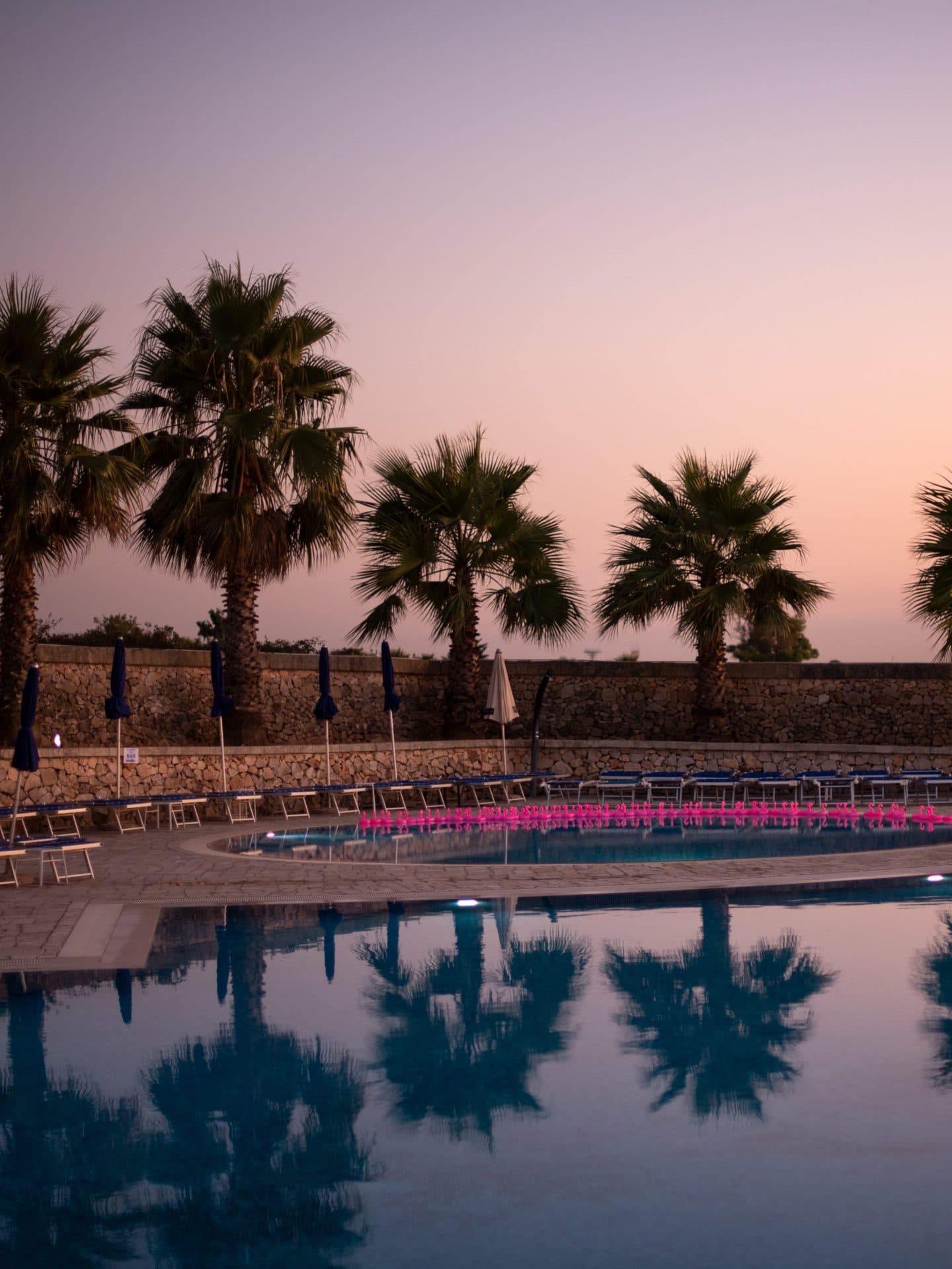 tramonto con cielo viola, sotto una piscina e di sfondo delle palme