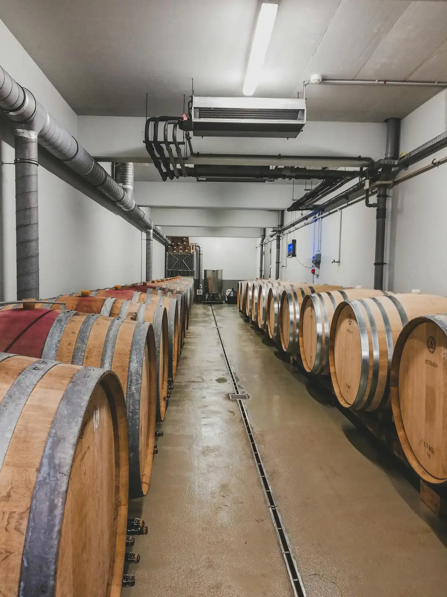 Horizontally aligned wooden barrels stored in an industrial warehouse setting.