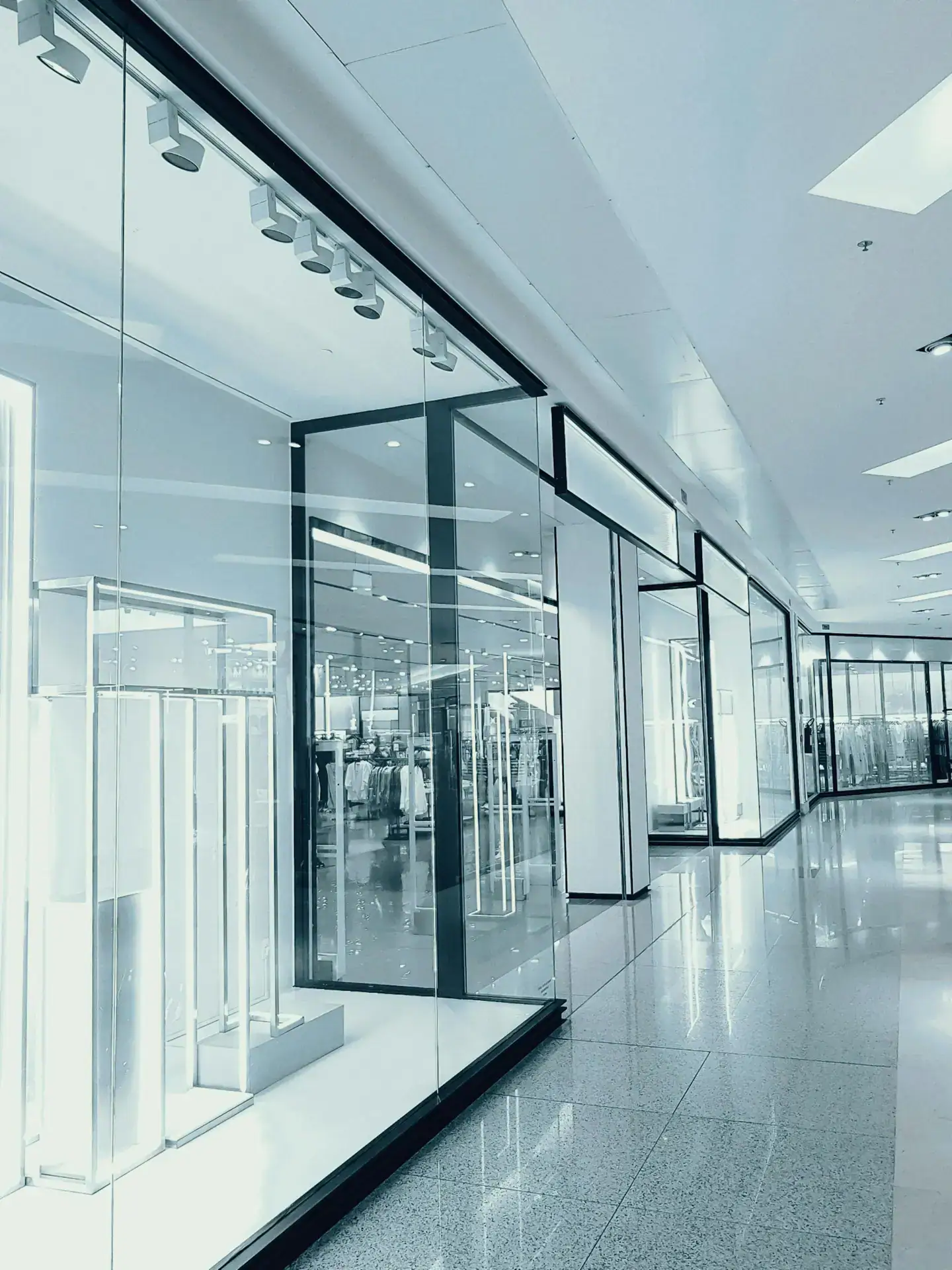 Bright and empty shopping mall corridor with glass display walls and reflections.