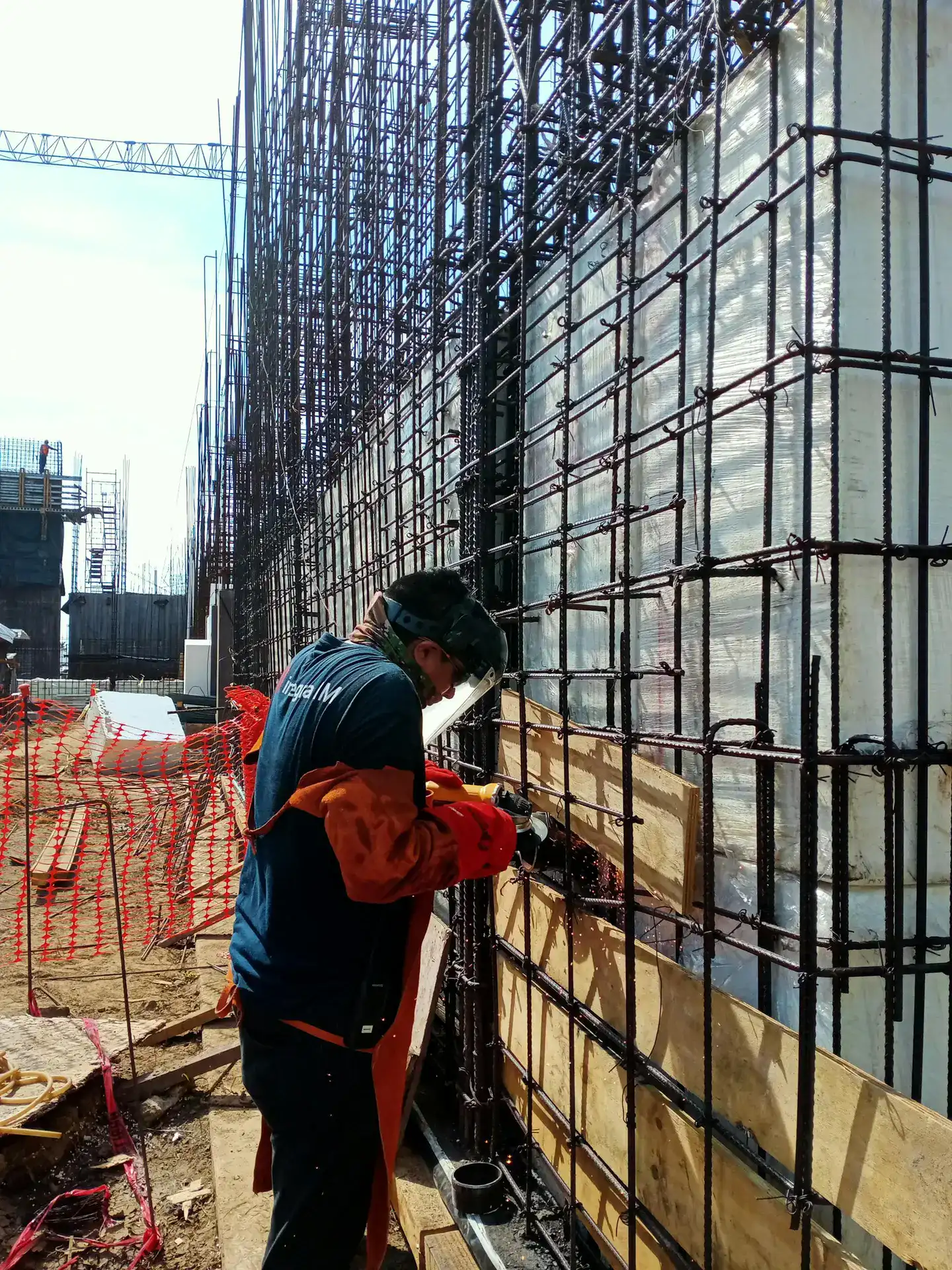 A construction worker welds metal frameworks at a busy building site, showcasing industrial safety.