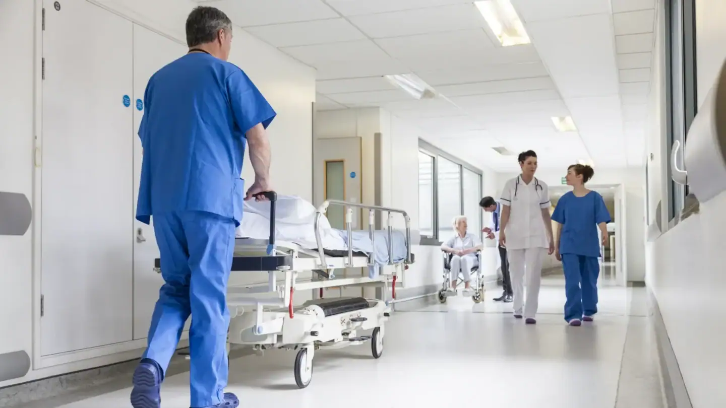 Hospital staff in healthcare sector moving a patient bed through a corridor while other staff walk nearby