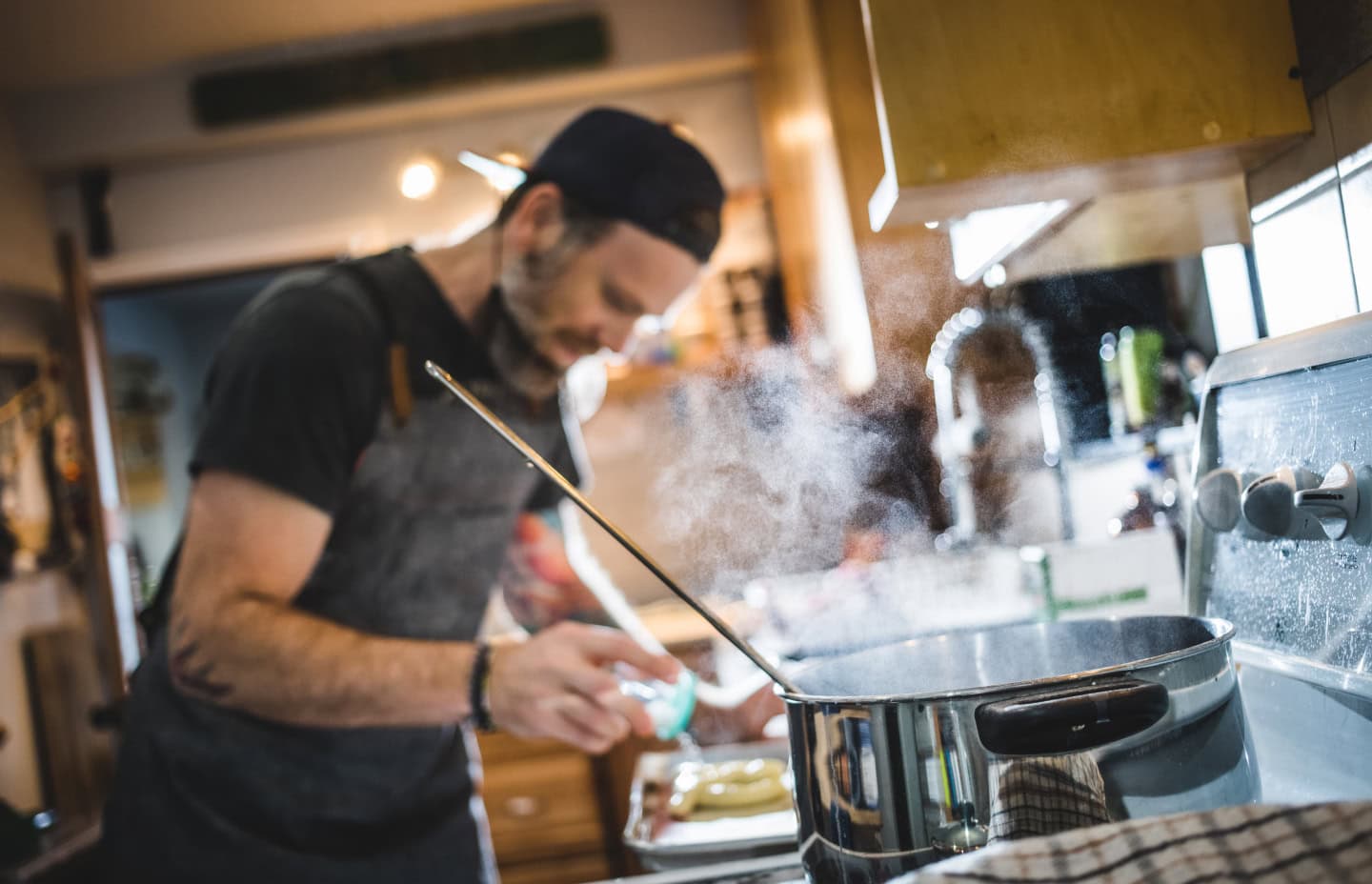 A man wearing an apron is skillfully cooking in a well-equipped kitchen, surrounded by various cooking utensils and ingredients