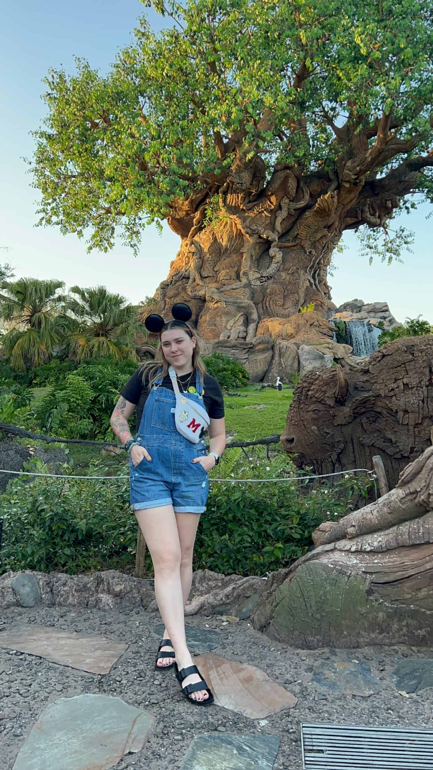 Vibrant Disney's Tree of Life at Animal Kingdom, lush greenery, and a young woman with Mickey Mouse ears enjoying Orlando Florida.