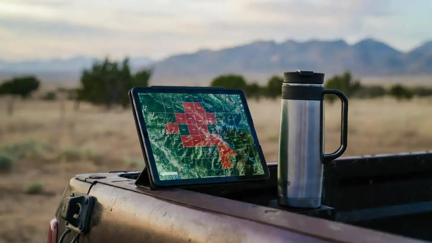 Tablet showing a highlighted county map on a pickup tailgate with ranch land in the background