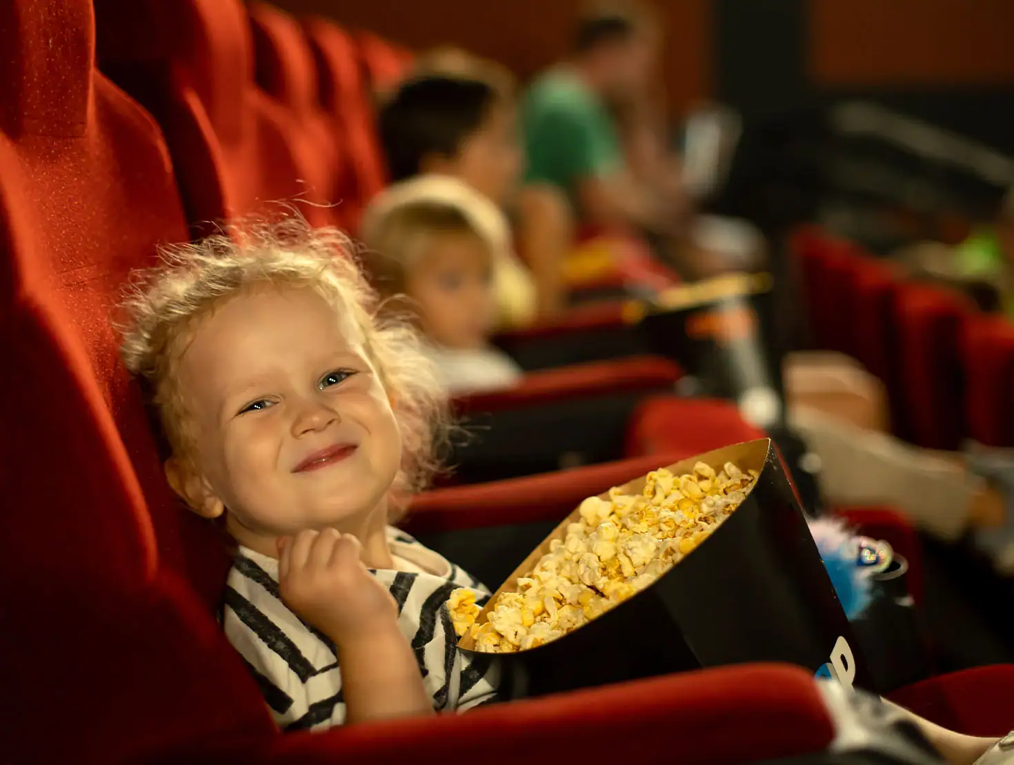 Criança atenta a ver um filme no cinema enquanto partilha um balde de pipocas com a mãe.