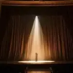 Actor rehearsing alone on a dimly lit stage with a single spotlight.