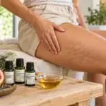 Donna che massaggia la coscia con cellulite visibile, accanto agli oli essenziali AMYRON di pompelmo, limone e ginepro.
