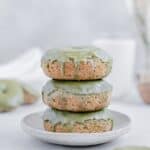 Three matcha glazed donuts stacked on a plate with a glass of milk in the background.