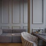 Уютная зона отдыха в ЖК Loftec: серые стены с классическими молдингами, низкий серый диван и белое плетёное кресло у рабочего стола — Кирилл Толль
