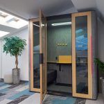 Высокий переговорный стол со светлыми барными креслами и подвесной акустической перегородкой на фоне кирпичной стены в БЦ Лотос, фотограф Кирилл Толль