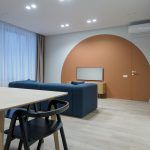 Интерьер кухни-гостиной в ЖК Западный порт: светлый обеденный стол с черными стульями, синий диван и скрытая дверь invisible, интегрированная в оранжевый круг. Москва, ЗАО.