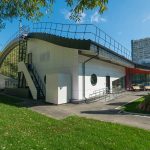 Перспективный вид на торцевой фасад с арочной крышей, эвакуационной лестницей и благоустроенным газоном у спорткомплекса                      