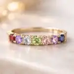 Gros plan sur une bague en or ornée de plusieurs pierres de naissance colorées disposées harmonieusement, lumière douce mettant en valeur les couleurs des gemmes.