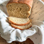 Fresh milled bread with Khorasan and hard white wheat in a basket with a neutral colored kitchen towel on top of a wooden table with wheat berries scattered around.